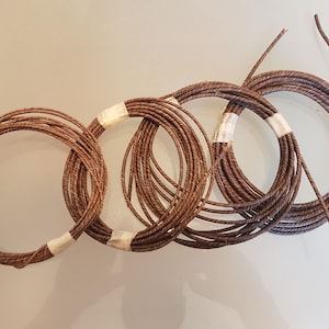 Könnte beinhalten: Drei Spulen braunes Garn, jede mit weißem Klebeband umwickelt.
