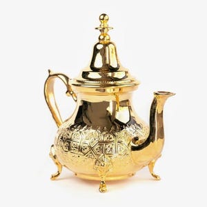 Könnte beinhalten: Eine goldfarbene Teekanne mit aufwendigen geprägten Mustern und einem gebogenen Ausguss. Die Teekanne hat einen Henkel und steht auf drei kleinen Füßen. Der Deckel ist mit einem dekorativen Knauf versehen. Die Teekanne ist wahrscheinlich aus Metall.