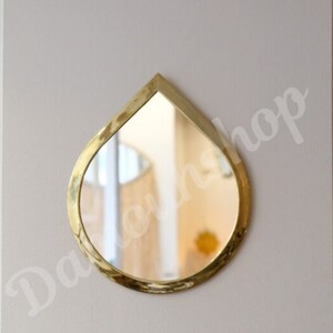 May include: A gold-coloured teardrop-shaped wall mirror with a bevelled edge.