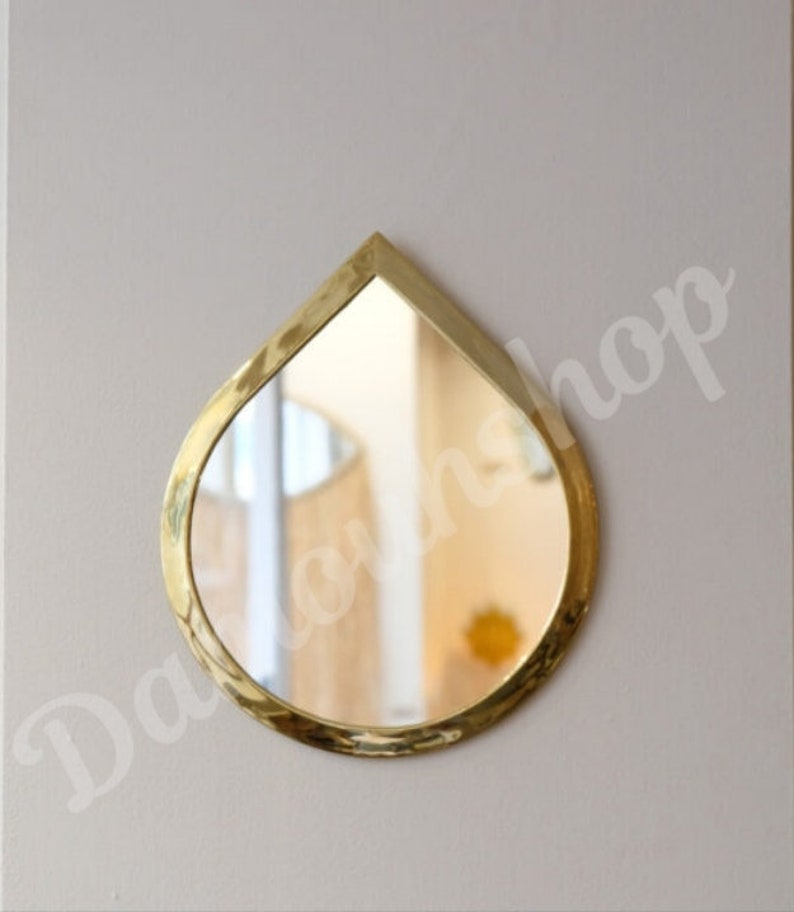 May include: A gold-coloured teardrop-shaped wall mirror with a bevelled edge.