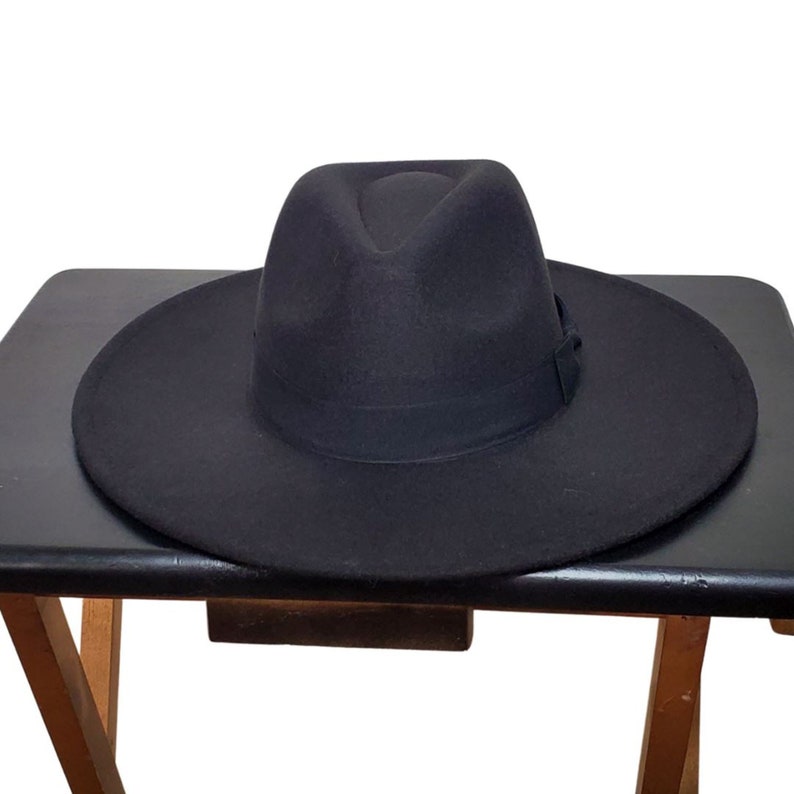Op de afbeelding: Een zwarte fedora hoed met een brede rand. De hoed is gemaakt van vilt en heeft een eenvoudig ontwerp.
