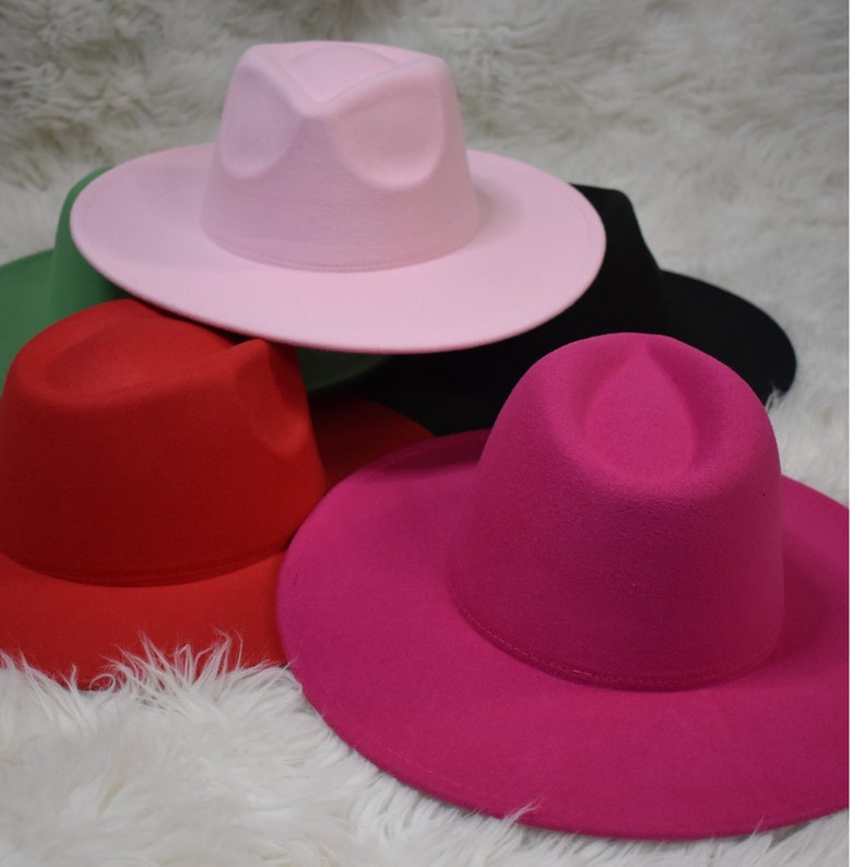 Op de afbeelding: Vier fedora-hoeden in verschillende kleuren: roze, rood, groen en fuchsia. De hoeden zijn gemaakt van vilt en hebben een brede rand.