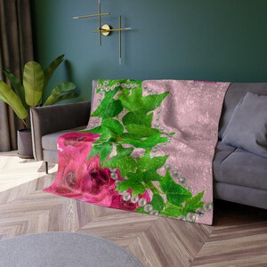 Op de afbeelding: Een roze en groene deken met een bloemenontwerp met roze rozen en groene bladeren met witte parel accenten.