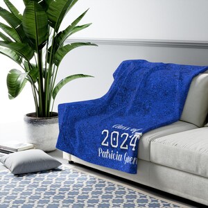 Op de afbeelding: Blauwe fleece deken met witte glitter. De deken heeft de tekst "Class of 2024" en "Patricia Gwen" erop gedrukt.