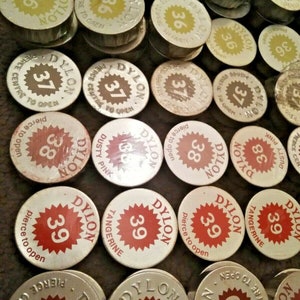 May include: A collection of round, metal dye tablets in various colours. Each tablet has a starburst design with the word "DYLON" and a number printed on it. The numbers range from 33 to 40.
