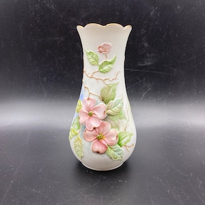 Może przedstawiać: Biały ceramiczny wazon z pozłacanym brzegiem i kwiatowym wzorem. Wazon przedstawia różowe i zielone kwiaty z liśćmi.