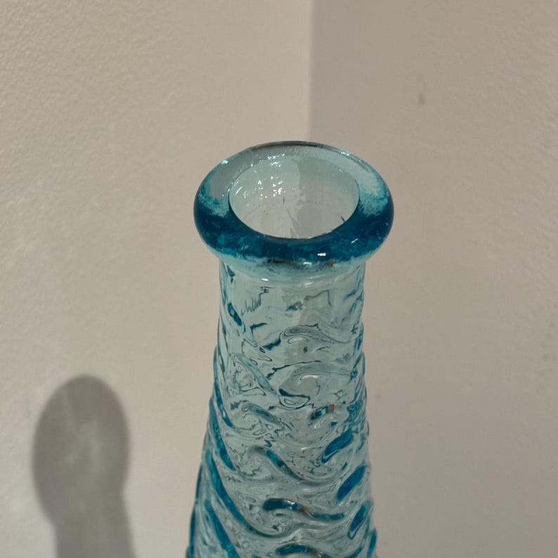 May include: A close-up of the top of a light blue glass bottle with a textured surface.