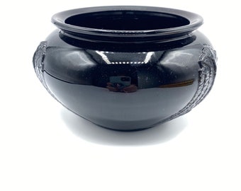 Può includere: Un vaso in ceramica nera con forma arrotondata e disegni intricati attorno al bordo. Il vaso è realizzato in un materiale lucido e ha una finitura liscia.