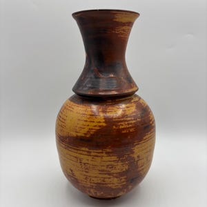 May include: A brown and yellow ceramic vase with a wide base and a narrow neck. The vase has a textured surface and a slightly flared lip.