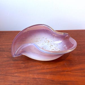 Peut inclure: Un bol décoratif en verre soufflé à la main, de forme organique. Le bol présente un dégradé de couleurs, passant d'un doux lavande à un intérieur blanc laiteux avec des mouchetures dorées. Le bord a un éclat irisé subtil.