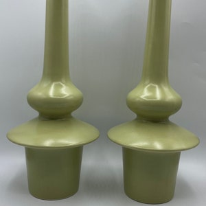 Op de afbeelding: Een paar groene keramische vazen met een uniek, bolvormig ontwerp. De vazen hebben een brede, platte basis en een smalle hals.