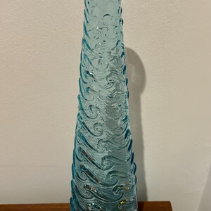 May include: A tall, light blue glass vase with a wavy, textured design. The vase is approximately 12 inches tall.