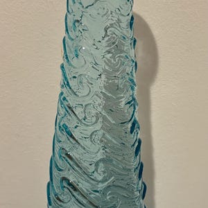 May include: A tall, clear blue glass vase with a swirling, textured design. The vase is shaped like a cone and has a wide base.