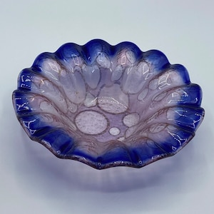 May include: A small, scalloped glass bowl with a purple and blue iridescent finish. The bowl has a textured, bubbly surface and a blue rim.