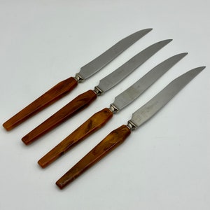 May include: Four stainless steel butter knives with brown plastic handles. The knives have a serrated edge and the handles have a marbled pattern.