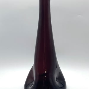 May include: A dark purple glass vase with a unique, organic shape. The vase has a narrow neck and a wide, rounded base.
