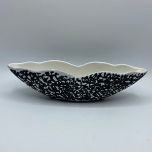 May include: A white ceramic bowl with a black speckled design. The bowl has a wavy, organic shape.
