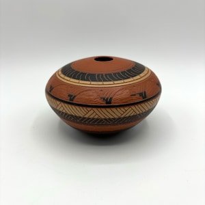 May include: A small, round, terracotta pottery vase with black and white geometric designs. The vase has a smooth, textured surface and a small opening at the top.