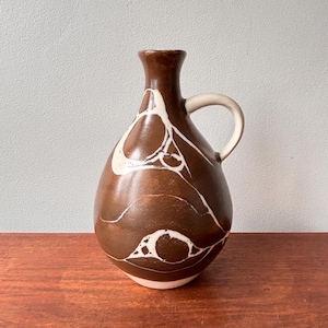 May include: A brown ceramic vase with a white marbled design and a handle. The vase has a rounded body and a narrow neck.