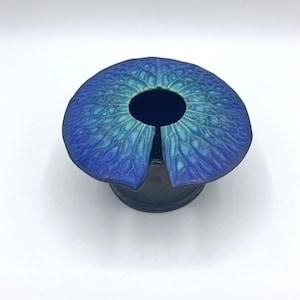 Puede incluir: Un jarrón de cerámica azul y verde con un diseño único y orgánico. El jarrón tiene una parte superior ancha y abierta y una base estrecha.