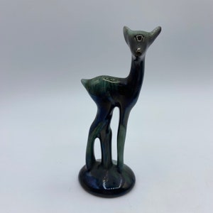 Puede incluir: Una figurita de cerámica de ciervo con un esmalte negro y verde. El ciervo está de pie sobre una pequeña base.