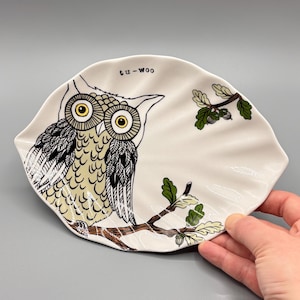 May include: White ceramic dish shaped like a leaf with a black and white owl perched on a branch with green leaves and acorns. The dish has the text "tu-woo" written on it.