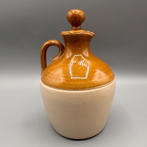 Peut inclure: Une cruche en céramique brune avec une base blanche et un couvercle brun. La cruche a une anse et un bec.