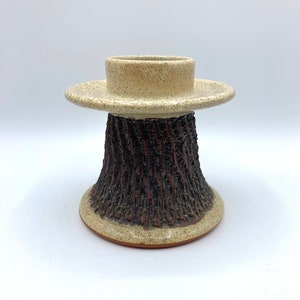 May include: A ceramic candle holder with a textured brown base and a white top. The base is designed to look like tree bark.