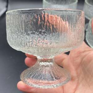 May include: Set of four clear glass dessert dishes with a textured, rippled surface. The dishes have a wide, shallow bowl and a tall, slender stem.