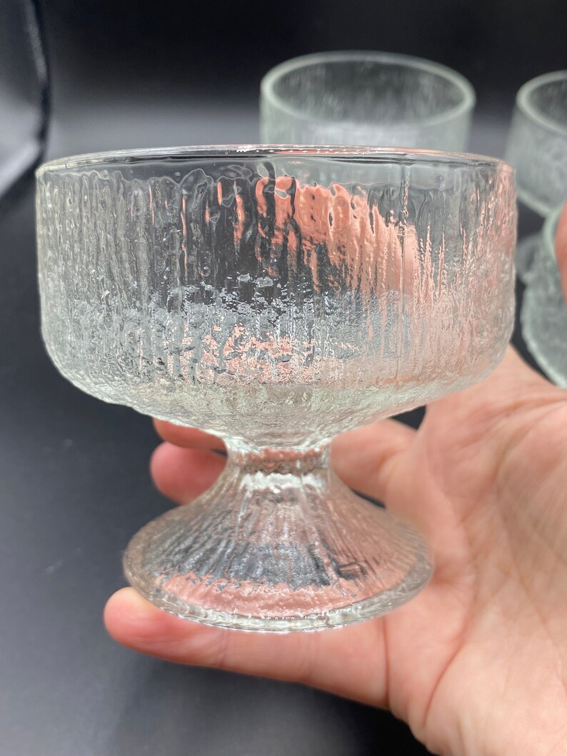 May include: Set of four clear glass dessert dishes with a textured, rippled surface. The dishes have a wide, shallow bowl and a tall, slender stem.