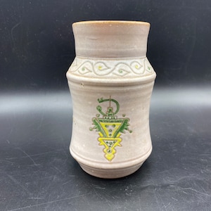 May include: A white ceramic vase with green and yellow geometric designs. The vase has a rounded base and a slightly flared top.