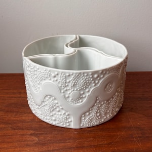 Może przedstawiać: Biała ceramiczna miska do serwowania z teksturowanym, wypukłym wzorem kropek i wirów. Miska ma trzy przegrody i jest okrągła. Miska stoi na drewnianej powierzchni.