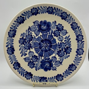 Könnte beinhalten: Ein weißer Keramikteller mit blauem Blumendesign. Der Teller hat einen weißen Hintergrund mit einem blauen Blumendesign am Rand und in der Mitte. Die Blumen sind blau und weiß und haben eine zarte, handgemalte Optik.