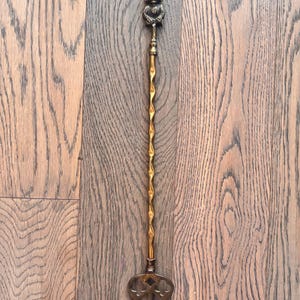 May include: A vintage brass serving fork with a decorative handle. The handle features a detailed figure at the top and a twisted design. The fork has three tines and an ornate design. The brass has a warm, aged patina.