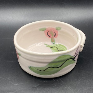 Peut inclure: Un bol en céramique blanche avec un motif de feuille verte et de fleur rose. Le bol a une petite poignée sur le côté.