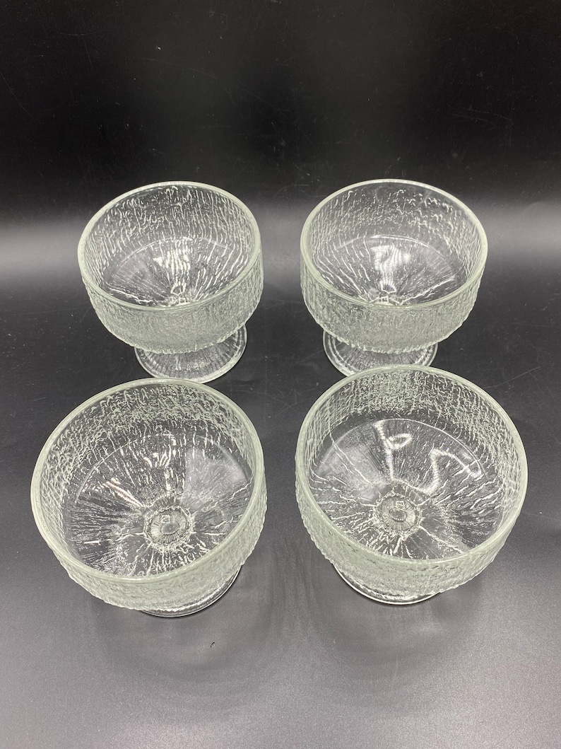 May include: Set of four clear glass dessert bowls with a textured, crackled surface. Each bowl has a short, round stem.