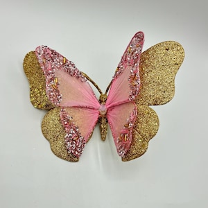 May include: A pink and gold glitter butterfly decoration. The butterfly has a pink sheer fabric body and gold glitter wings.