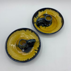May include: Two yellow ceramic candle holders with blue glaze. Each holder has a small, round candle cup with a handle.