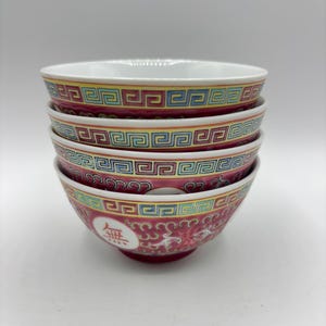May include: Four stacked red and white porcelain bowls with a gold and blue geometric pattern and a gold Chinese character.