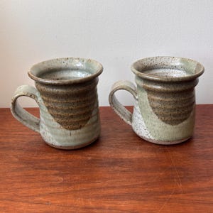 May include: A white ceramic mug with a black handle and the text "But First, Coffee" in a handwritten style. The mug is on a white surface. The mug is approximately 10 cm tall.
