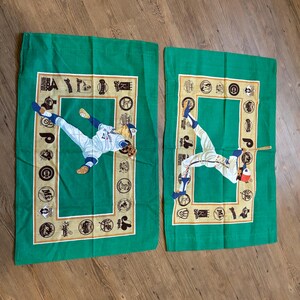 May include: Two green pillowcases with a baseball theme. Each pillowcase features a baseball player in action, surrounded by a border of baseball team logos. The logos are in gold and white on a green background.