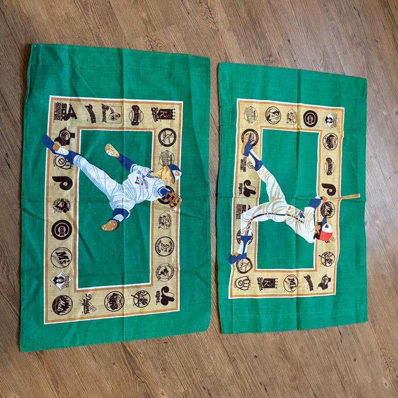 May include: Two green pillowcases with a baseball theme. Each pillowcase features a baseball player in action, surrounded by a border of baseball team logos. The logos are in gold and white on a green background.