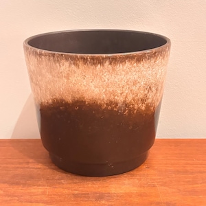 May include: A ceramic plant pot with a layered design. The top is a light beige colour, transitioning to a brown band, and ending with a dark brown base. The interior is dark brown.