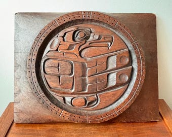 May include: A carved wooden wall art piece featuring a detailed relief of a bird within a circular frame. The artwork is a warm brown color, with intricate carvings and a textured background. The piece is displayed on a wooden surface.