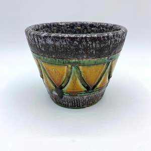 May include: A small, brown and green ceramic planter with a geometric pattern. The planter has a textured surface and a slightly flared rim.