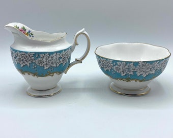 May include: A white cream jug and sugar bowl set with a blue and white floral pattern. The cream jug has a handle and a spout. The sugar bowl is round.