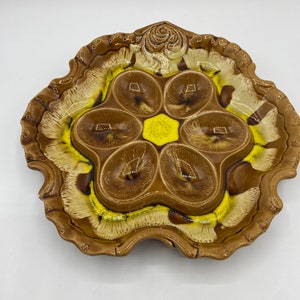 May include: A brown and yellow ceramic serving dish with six individual compartments. The dish is shaped like a flower with a raised center and scalloped edges.