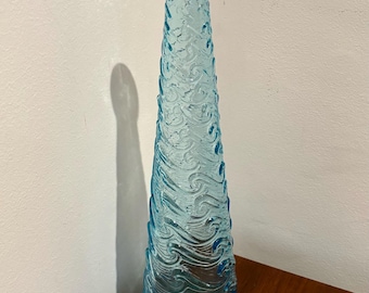 May include: A tall, light blue glass vase with a textured wave design. The vase is empty and has a rounded bottom.
