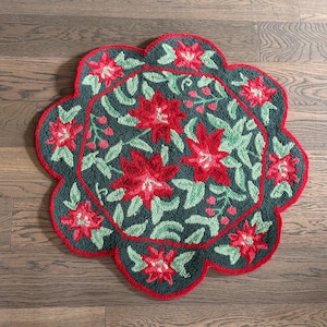 May include: A round, floral-patterned rug with a scalloped edge. The rug features a dark teal background with red poinsettias and green leaves. The edge and inner border are red, creating a festive holiday theme.