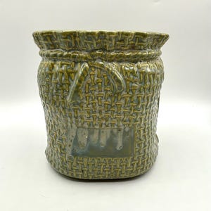 May include: A green ceramic planter shaped like a woven sack with a textured surface.